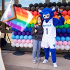 Victor E Bull posing with a student in front of a balloon progress pride wall. 