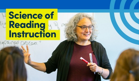 Person standing in front of dry erase board holding markers and talking to class.