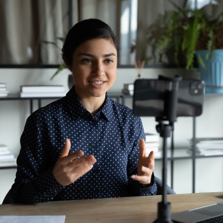 Royalty-free stock photo ID: 1694217805 Smiling indian ethnic girl sitting in front of smartphone on stabilizer, recording self-presentation video or sharing professional skills. Happy young smart businesswoman filming educational lecture.