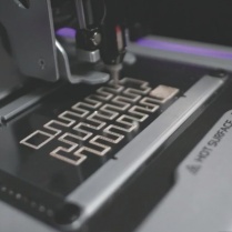 close-up of a precision machine with a nozzle depositing patterns on a metal surface. 