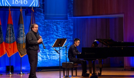 Two musicians perform on stage. One plays the clarinet, and the other plays the piano.