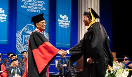 President Satish K. Tripathi shakes hands with a graduate as they cross the stage. 