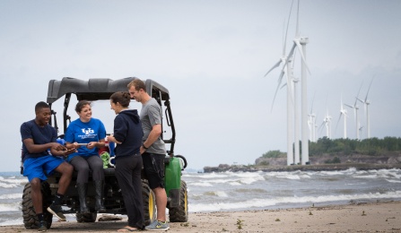 students collecting samples at Woodlawn Beach with wind turbines in the distance.