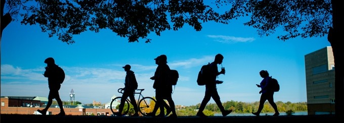 students walking on campus, silhouetted against a blue sky.