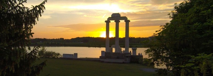The three columns of Baird Point and nearby evergreen trees are silhouetted by a bright yellow half-set sun and night blue sky.