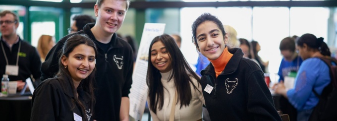 3 Student Engagement Ambassadors wearing their signature black fleeces, pose with a student mentor while networking during a morning session.
