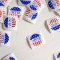 Red, white, and blue "I Voted" stickers are scattered about a white table. 