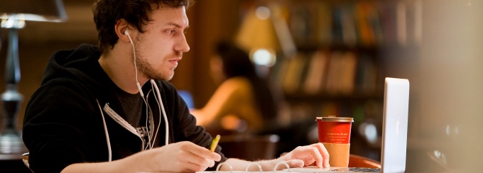 A student studying in the library with coffee and earbuds.