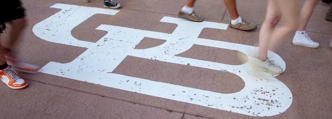 Students feet walking by white interlocking UB symbol on the ground. 