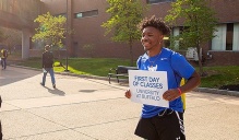 A student get a photo taken while holding a sign reading, "First Day of Classes.". 