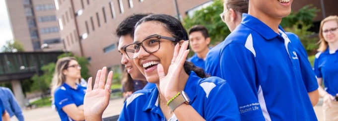 Four orientation leaders stand in the middle of a group circle during a game at a summer orientation session. All orientation leaders are wearing a version of khaki pants or shorts and their signature UB blue and white polos.