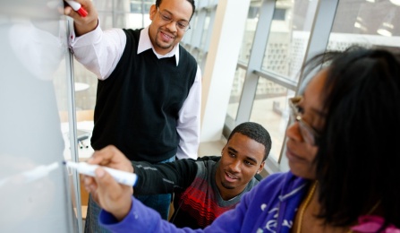 Assistant professor overlooks students writing on a white board.