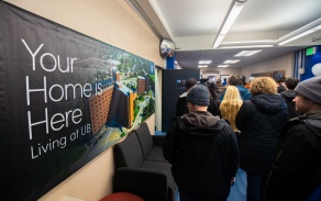 Photo of students walking down a hall at Goodyear Hall. A sign on the wall says, "Your Home Here: Living at UB.". 