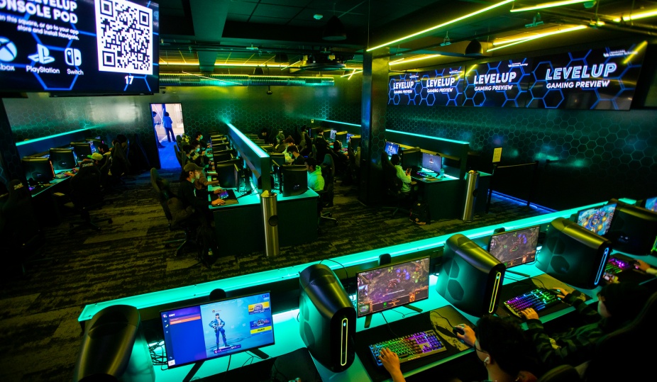 The interior of LevelUp, showing a room full of computer consoles with students at the computers. The room is dark with green backlights from the computing set up. 