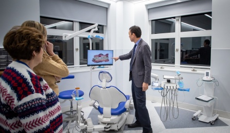 Photo of a dental chair and dental equipment, and a person pointing to a screen. 