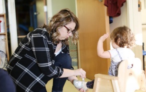 Photo of toddler child and teacher helping to put shoe on.