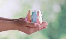 A photo of a circle of paper dolls in different colored paper held in a person's hands. 