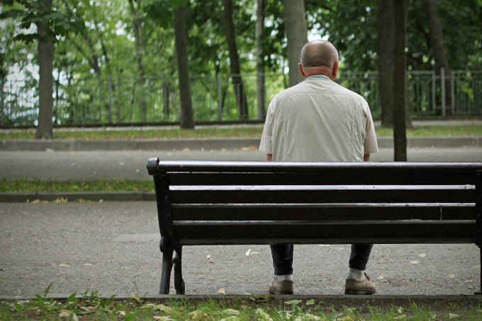 Elderly man sitting by himself on a park bench. 