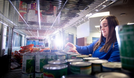A person stocks shelves with canned goods.
