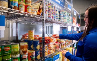 Student in blue jacket organizing food on shelves at Blue Table food pantry. 