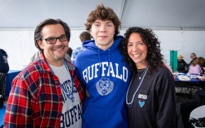 UB student in between two parents inside the tailgate tent. 