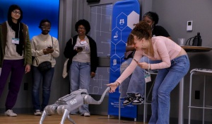 A girl excitingly shaking the hand of a robot dog.